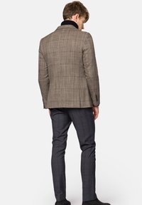 Brązowa blazer w kratkę z wysokim kołnierzem, zestawiona z ciemnoniebieskimi spodniami w kratkę. Teksturowana tkanina i dopasowany krój.