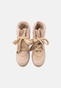 Ζευγάρι μπεζ σουέντ αθλητικών παπουτσιών ψηλού τύπου με φαρδιές κορδόνες δεμένες σε φιόγκους, σε άποψη από ψηλά πάνω σε λευκό φόντο.