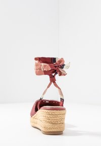 Espadrille-Sandale mit einem gewebten roten Obermaterial, Jutewedge-Absatz und einem gemusterten Textil-Fußgelenkband, das zu einer Schleife gebunden ist. Glatte Sohle und strukturierter Grip.