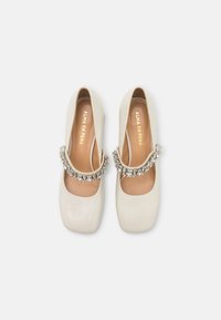 Scarpe Mary Jane in pelle verniciata bianca con punta quadrata, cinturino decorato con strass e interno beige con il nome del marchio.