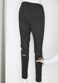 Zwarte sportbroeken met een elastische tailleband, taps toelopend ontwerp, zijzakken en reflecterende accenten nabij de onderbenen.