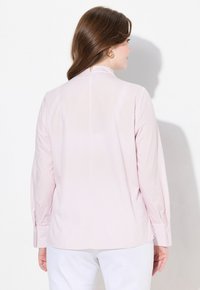 Camicia rosa chiaro a maniche lunghe con righe verticali bianche, vista dal retro. Presenta un colletto, polsini con bottoni e un piccolo dettaglio di spacco sul retro.