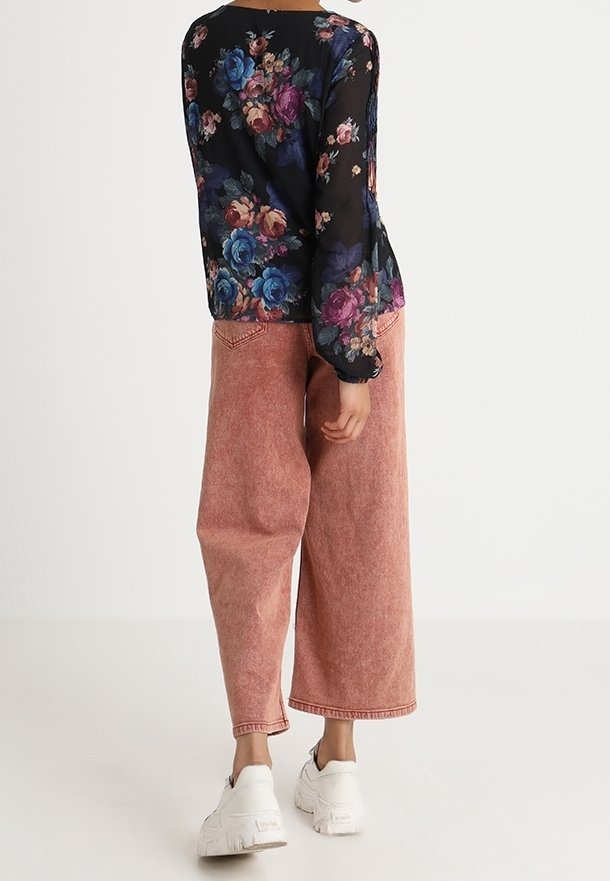 Blumenmuster durchsichtige Bluse in Schwarz mit blauen und rosa Rosen, kombiniert mit hoch taillierten, lockeren rosa Jeans und weißen klobigen Sneakern.