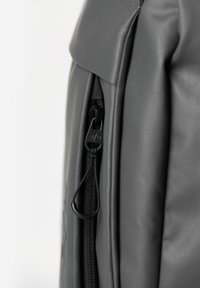 Grijze rugzak met een elegante, gestructureerde buitenkant. Voorzien van een zwarte rits met een trekband en subtiele branding aan de zijkant.