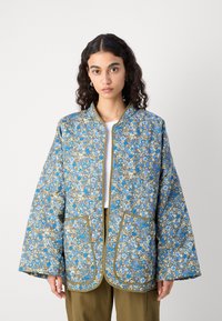 Giacca trapuntata con motivo floreale in blu e beige, con rifiniture dorate, maniche ampie e due tasche frontali.