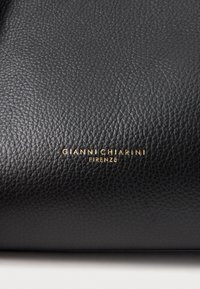 Melnas ādas soma ar teksturētu virsmu un zelta iegravētu logotipu "GIANNI CHIARINI FIRENZE" netālu no apakšējās malas.