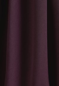 Tissu violet foncé avec des plis verticaux doux et une surface lisse légèrement texturée.