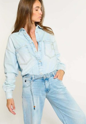 Lichtblauwe denimshirt met een knoopsluiting aan de voorkant, twee borstzakken en een relaxte pasvorm, gecombineerd met bijpassende lichtblauwe jeans.