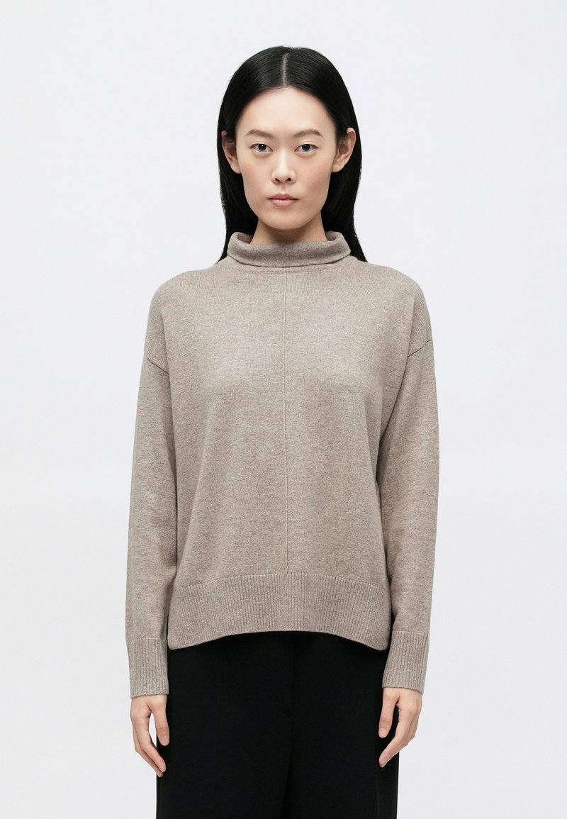 Μπεζ φαρδιά πουλόβερ με ζιβάγκο από μαλακό πλεκτ�ό υλικό, με ριμπ τελείωμα και μανσέτες, εμφανιζόμενο σε απλό φόντο.