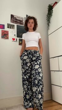 Weißes Crop-Top und marineblaue, weite Blümchen-Hosen mit weißen und grünen Blumenmustern. Die Hose hat einen elastischen Bund und Seitentaschen.