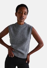 Pull sans manches gris avec un col côtelé haut et un ourlet côtelé, fabriqué à partir d'un matériau tricoté doux et texturé.