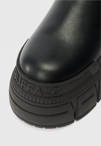 Botas de plataforma pretas com um cabedal de couro liso e sola de borracha texturizada, apresentando o nome da marca "BUFFALO" estampado na lateral.