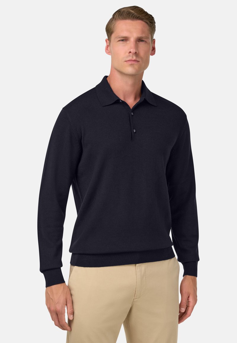 Jūras spēku tumši zils garā piedurkne polo krekls no teksturēta auduma, ar klasisku apkakli un trīs pogu aizdari, apvienots ar gaišas krāsas biksēm.