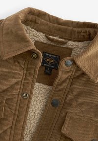 Veste en velours côtelé marron avec doublure en sherpa polaire, fermeture par boutons, poche poitrine et étiquette indiquant la taille moyenne et les détails de la marque.