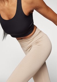 Top deportivo negro recortado combinado con leggings beige de talle alto con textura y sutiles rayas verticales.