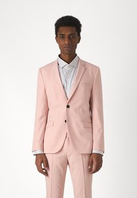 Abito rosa con colletto a punta, chiusura con un solo bottone e due tasche frontali. Camicia bianca con colletto e patta dei bottoni sottostante.