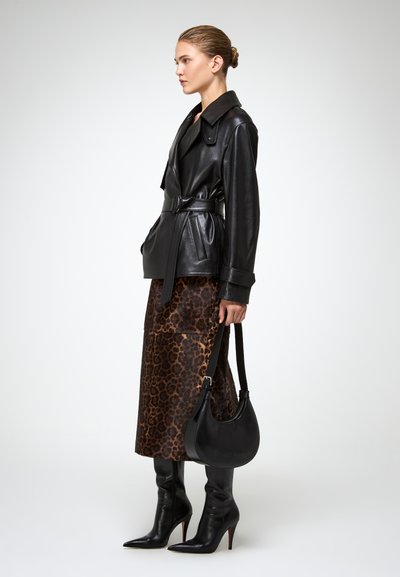 Zwarte leren jack met riem, gecombineerd met een midi-rok met luipaardprint en zwarte kniehoge stiletto-laarzen, een zwart halve maan handtas vasthoudend.