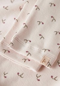 Textuur roze stof met een ribbelpatroon en verspreide bloemenmotieven in paars en bruin. Bevat een klein label aan de rand.