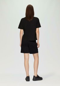 Schwarzes Kurzarm-Shirt und schwarze Shorts mit lockerer Passform und glattem Stoff, kombiniert mit schwarzen Sneakers, von hinten betrachtet.