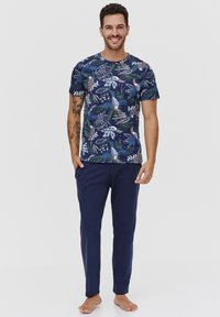 Granatowa koszulka z kolorowym tropikalnym wzorem liści; połączona z ciemnoniebieskimi spodniami. Tkanina wydaje się miękka, a krój jest luźny.