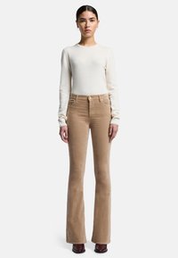 Lichtcrème trui en beige flared corduroy broek. De broek heeft een gladde textuur en een klassiek vijf-pocketdesign. Bruine enkellaarsjes met hak.