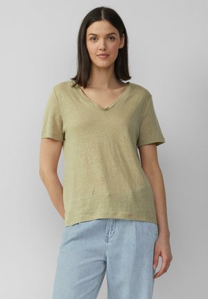 Oliwkowa, krótkim rękawem koszulka typu V-neck, wykonana z miękkiego, teksturowanego materiału, połączona z jasnoniebieskimi dżinsami. Prosty i klasyczny design.