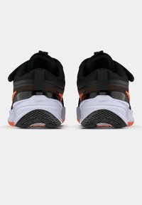 Μαύρα αθλητικά παπούτσια με γυαλιστερό μαύρο λουρί, πορτοκαλί λεπτομέρειες και υφή άσπρης σόλας με μαύρο σχέδιο τριχιάς.