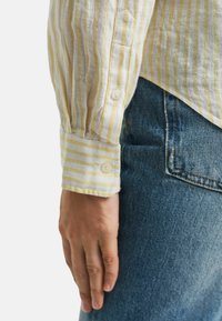 Licht gestreepte gele en witte shirt met een knoopmanchet. De stof lijkt textuur en casual te zijn. Draag het met een blauwe spijkerbroek.