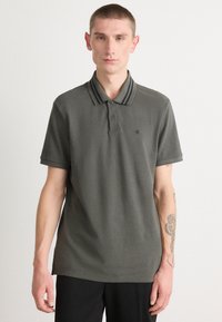Tmavě zelené polokošile s proužkovaným límcem. Vyrobeno z texturované tkaniny, má zapínání na knoflíky a decentní logo na hrudi.