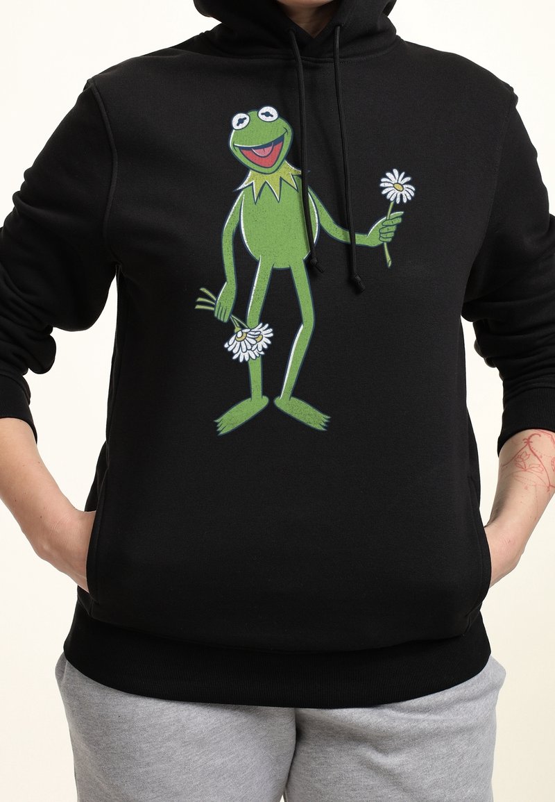 Haut à capuche noir avec un personnage de grenouille verte imprimé tenant des marguerites, avec un cordon de serrage au niveau de la capuche et des poignets et un ourlet côtelés.