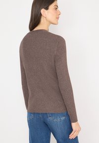 Brązowy sweter z prążkowanej dzianiny z długimi rękawami, okrągłym dekoltem i lekko dopasowanym krojem, w zestawieniu z niebieskimi jeansami.