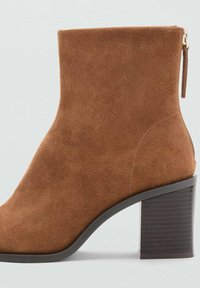Stivaletto in suede marrone con cerniera laterale e tacco a blocco impilato su uno sfondo grigio chiaro.