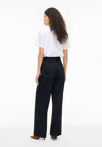 Mørkeblå jeans med vide ben og høyt liv, kombinert med en hvit t-skjorte. Tydelige baklommer og glatt, solid denimstruktur.