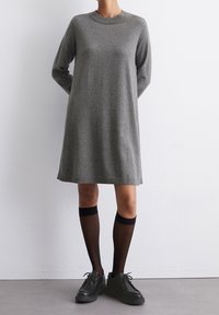 Abito maglione grigio a maniche lunghe con scollatura arrotondata, caratterizzato da una vestibilità comoda. Indossato con calze nere fino al ginocchio e scarpe con plateau nere.
