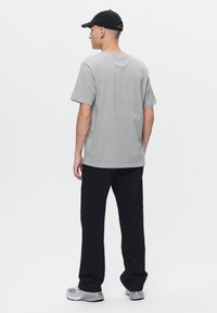 T-shirt di cotone grigio con maniche corte, abbinata a pantaloni neri. L'individuo indossa un cappellino nero e sneakers grigie, visto di spalle.