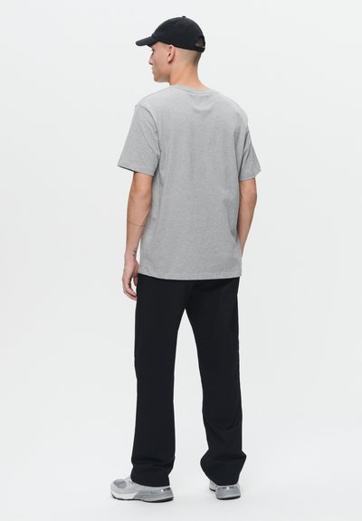 Gray cotton t-shirt with short sleeves, paired with black pants. The individual wears a black cap and gray sneakers, viewed from behind.