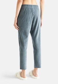 Ljusblå, vertikalt randiga corduroypants med elastiskt midjeband. Mjuk känsla. Bärs med vita, fluffiga tofflor.