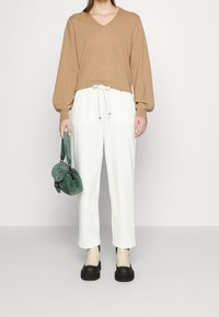 Beige v-kaulusneule, valkoiset elastisella vyötäröllä varustetut housut, mustat platform-kengät ja pieni vihreä tekoturkishandbag. Yksinkertainen, moderni ilme.