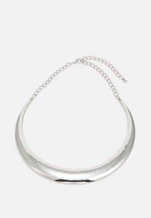 Collier ras du cou argenté en forme de croissant avec chaîne ajustable et fermoir mousqueton sur fond clair.