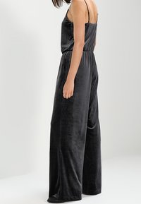 Combishort en velours noir avec des bretelles spaghetti, des jambes larges et une taille élastique. Texture lisse avec un léger éclat. Pas de détails matériels visibles.