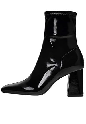 Bottine noire à la brillance élevée, avec un bout pointu élégant, un empeigne élastique et un talon carré épais. Texture lisse et design ajusté.