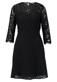 Robe en dentelle noire avec manches trois-quarts, motif floral, corsage ajusté, jupe évasée, et décolleté arrondi. Superposition de dentelle texturée.