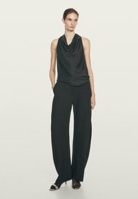 Top senza maniche in satin verde scuro con scollatura a cowl abbinato a pantaloni larghi neri. Le scarpe presentano un design in nero e argento.