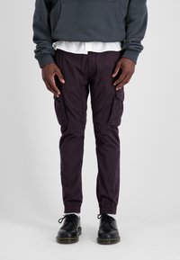 Donkerpaarse cargo-broek met zijzakken, tapered fit, elastische boorden, gecombineerd met een grijze hoodie en zwarte veterschoenen.