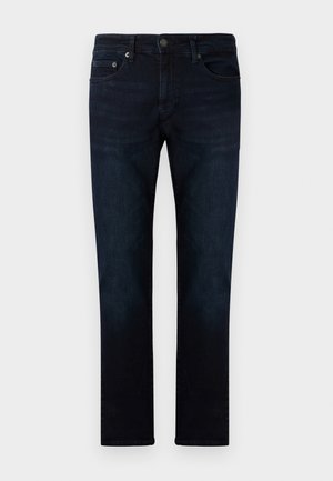 Tamno plave traperice s ravnim krojem, koje imaju prednje džepove, suptilnu teksturu izbljeđenja i metalno dugme za zatvaranje na pojasu.