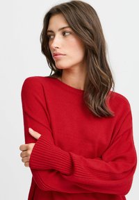 Rode gebreide trui met een losse pasvorm, geribde manchetten en een brede halslijn. Zachte textuur met lange mouwen, die warmte en comfort biedt.
