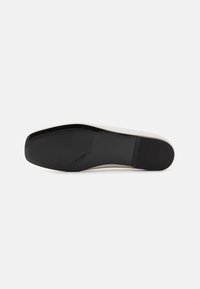 Svart gummisåle av en sko med en glatt hvit kropp, som har en strømlinjeformet, langstrakt form og minimal merkevare på undersiden.