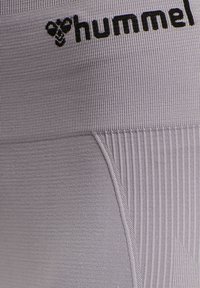 Hummel leggings in lichtgrijs, met een geribbelde textuur, gladde stof en een zwart logo op de tailleband.
