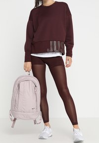 Bordowy sweterek z prążkowanym wzorem z napisem "JUST", czarne szorty, jasnoróżowy plecak i białe sneakersy. Gładkie materiały z sportowym designem.