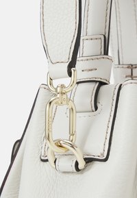 Detail van een witte leren tas met gouden hardware. De riem heeft zwarte randen en contrasterende stiksels, die het gestructureerde ontwerp benadrukken.